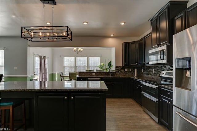 kitchen with an inviting chandelier, decorative light fixtures, a center island, dark stone countertops, and stainless steel appliances