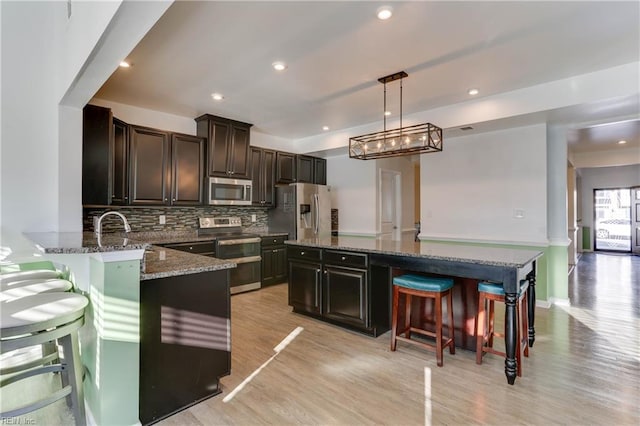 kitchen with stainless steel appliances, decorative light fixtures, a kitchen island, and backsplash