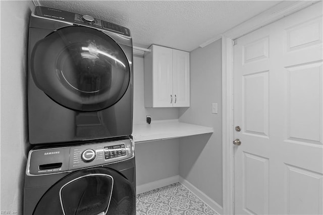 laundry area with cabinets, stacked washer and dryer, and a textured ceiling