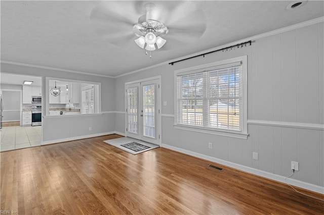 unfurnished living room with french doors, crown molding, ceiling fan, and light hardwood / wood-style flooring