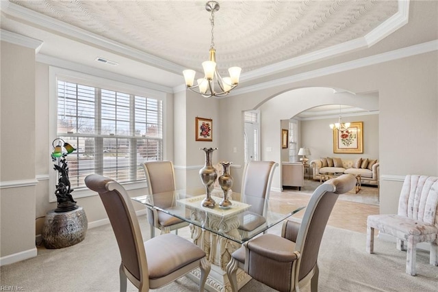 carpeted dining space with a raised ceiling, ornamental molding, and a notable chandelier