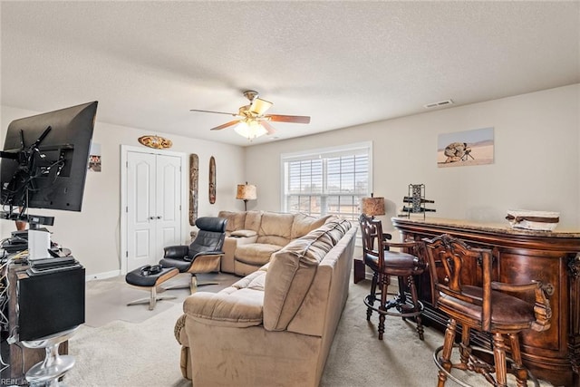 living room with ceiling fan, bar, light colored carpet, and a textured ceiling