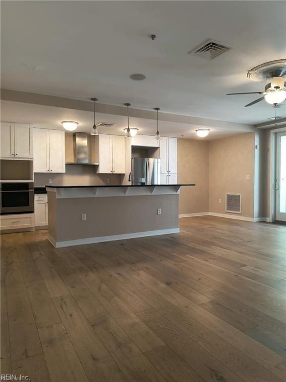 kitchen with white cabinetry, decorative light fixtures, wall chimney exhaust hood, and appliances with stainless steel finishes