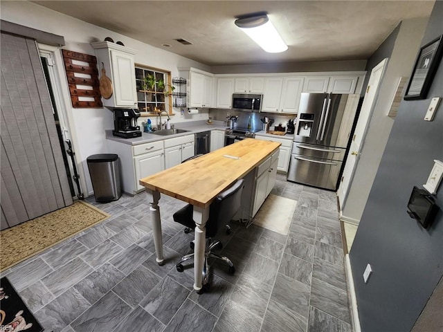 kitchen with appliances with stainless steel finishes, butcher block counters, sink, and white cabinets