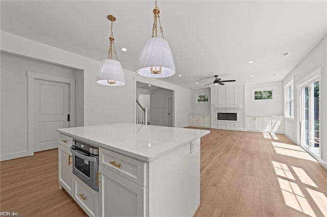 kitchen featuring pendant lighting, white cabinetry, light hardwood / wood-style floors, a kitchen island, and stainless steel oven