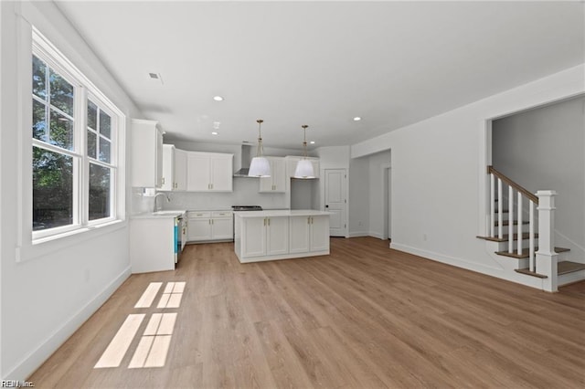 kitchen with decorative light fixtures, a center island, white cabinets, light hardwood / wood-style floors, and wall chimney range hood