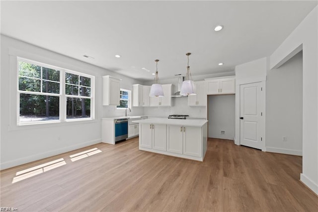 kitchen with dishwasher, a kitchen island, white cabinets, pendant lighting, and wall chimney range hood