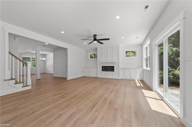 unfurnished living room featuring ceiling fan with notable chandelier, a fireplace, and light hardwood / wood-style floors