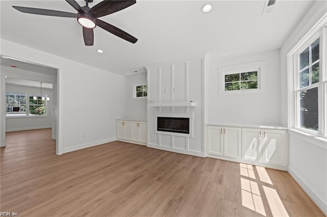 unfurnished living room with a large fireplace, ceiling fan with notable chandelier, and light hardwood / wood-style flooring