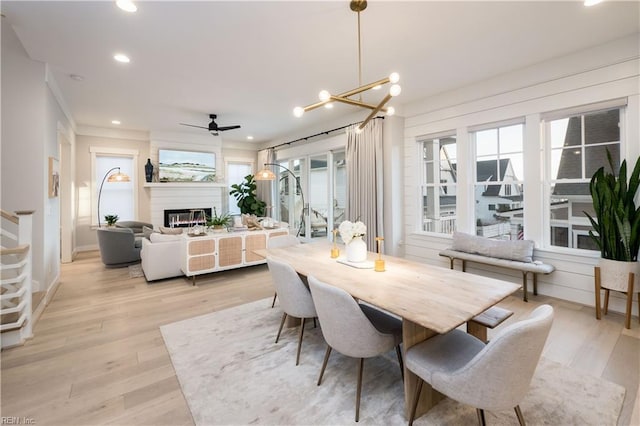 dining area featuring a large fireplace, ceiling fan with notable chandelier, and light wood-type flooring