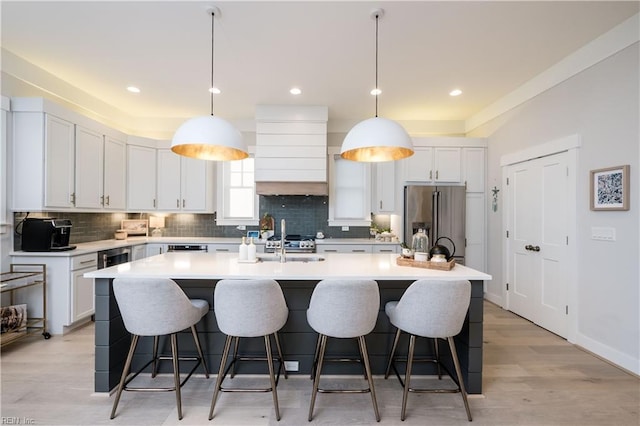 kitchen featuring premium range hood, high end refrigerator, hanging light fixtures, a kitchen island with sink, and white cabinets