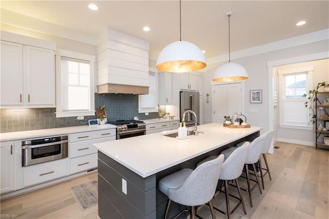 kitchen with white cabinetry, appliances with stainless steel finishes, sink, and a center island with sink