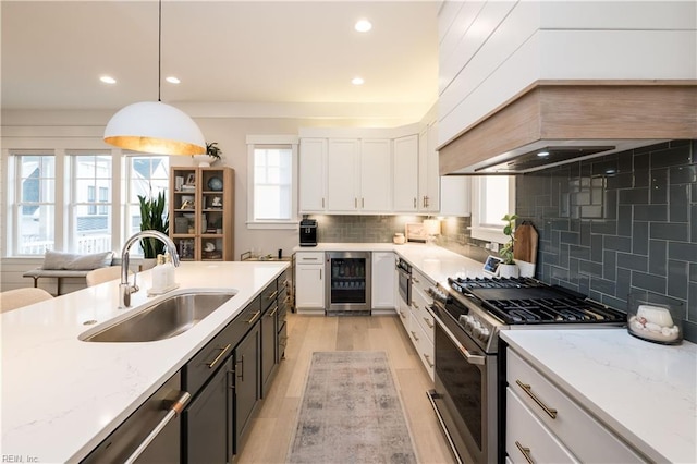 kitchen featuring sink, hanging light fixtures, white cabinets, gas range, and beverage cooler