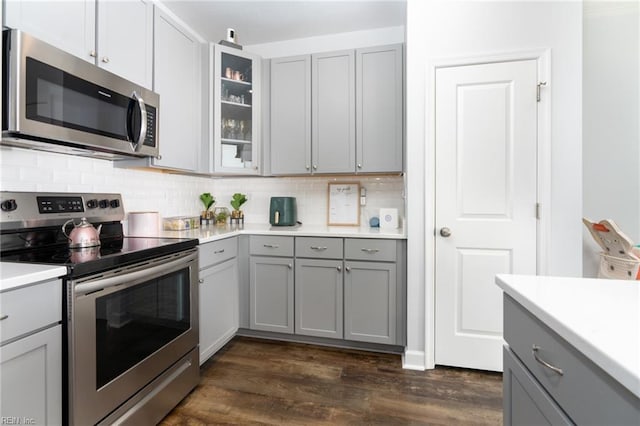 kitchen with dark wood-type flooring, stainless steel appliances, decorative backsplash, and gray cabinetry