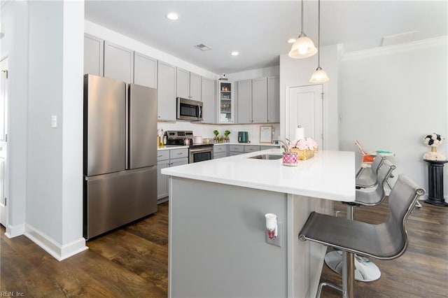 kitchen with sink, appliances with stainless steel finishes, a kitchen breakfast bar, gray cabinets, and pendant lighting