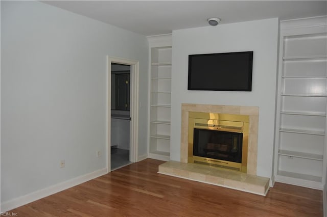 unfurnished living room featuring built in features, wood-type flooring, and a tile fireplace