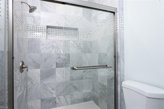 bathroom with a shower with shower door and toilet