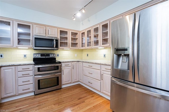 kitchen featuring backsplash, appliances with stainless steel finishes, light stone counters, and light wood-type flooring