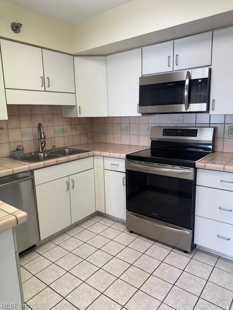 kitchen featuring stainless steel appliances, white cabinetry, tasteful backsplash, and tile countertops