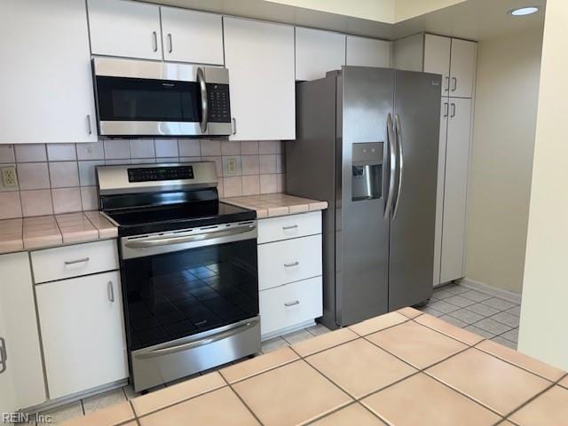 kitchen with white cabinetry, appliances with stainless steel finishes, tile countertops, and decorative backsplash