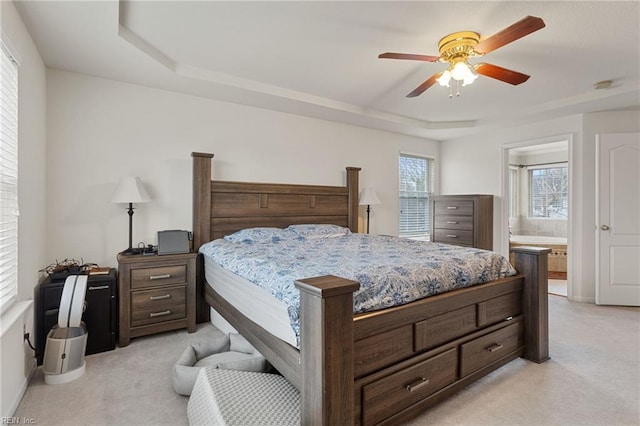 carpeted bedroom with ensuite bath, a raised ceiling, and ceiling fan