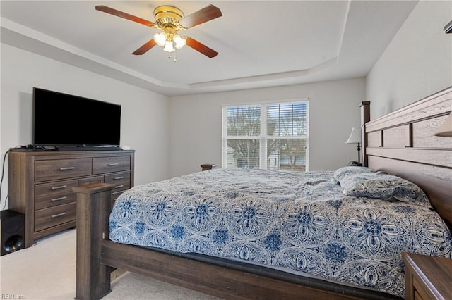 bedroom featuring ceiling fan, a tray ceiling, and light carpet