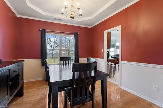 dining room featuring an inviting chandelier, crown molding, a raised ceiling, and light wood-type flooring