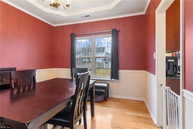 dining room featuring an inviting chandelier, a tray ceiling, light hardwood / wood-style floors, and crown molding