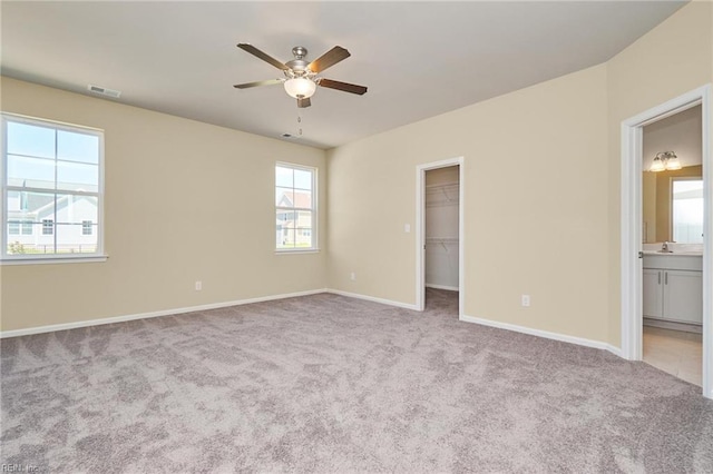 unfurnished bedroom featuring connected bathroom, a walk in closet, light colored carpet, and ceiling fan