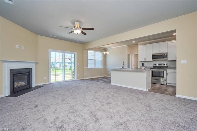 unfurnished living room featuring ceiling fan with notable chandelier and dark colored carpet