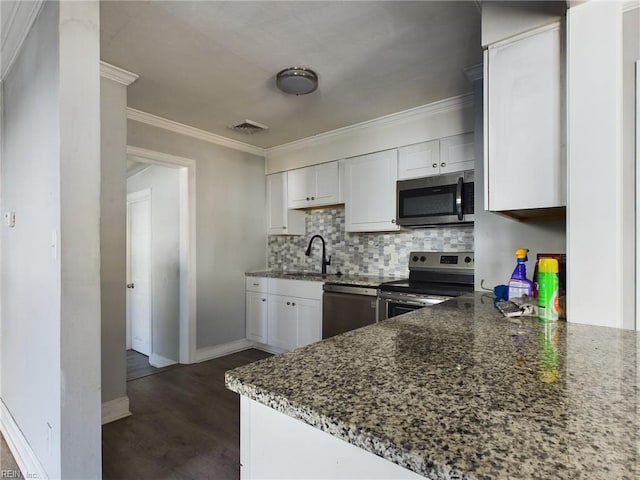 kitchen featuring appliances with stainless steel finishes, white cabinetry, backsplash, dark stone countertops, and ornamental molding