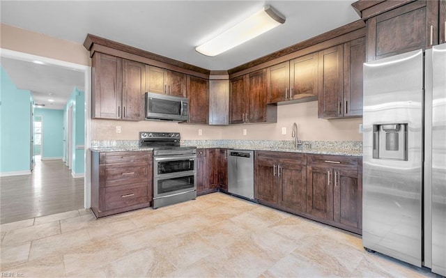 kitchen with light stone counters, dark brown cabinetry, stainless steel appliances, and sink