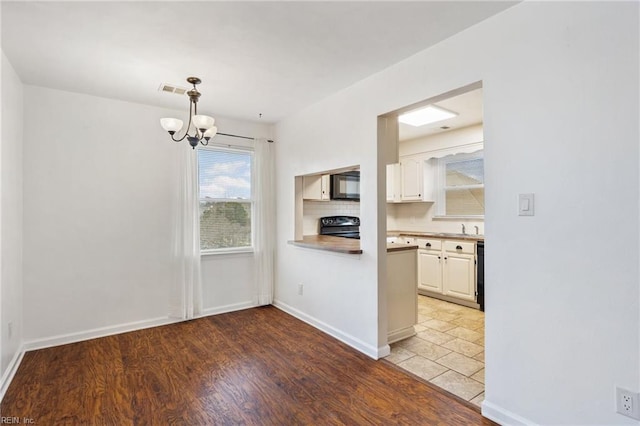 kitchen with sink, white cabinetry, hanging light fixtures, black appliances, and light hardwood / wood-style floors