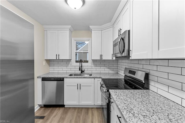 kitchen with stainless steel appliances, light stone countertops, sink, and white cabinets