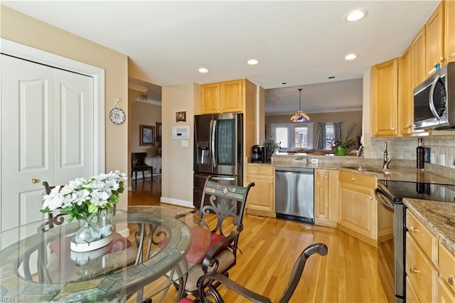 kitchen featuring stainless steel appliances, hanging light fixtures, and light brown cabinets