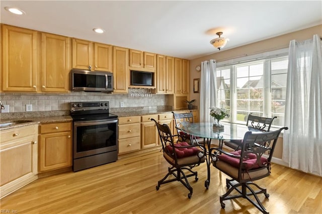 kitchen with sink, light stone counters, light hardwood / wood-style flooring, appliances with stainless steel finishes, and backsplash