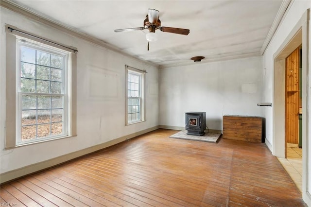 empty room featuring ornamental molding, a wood stove, ceiling fan, and light hardwood / wood-style flooring