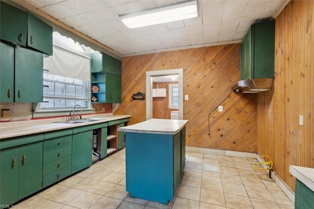 kitchen with wood walls, sink, a center island, green cabinets, and light tile patterned floors