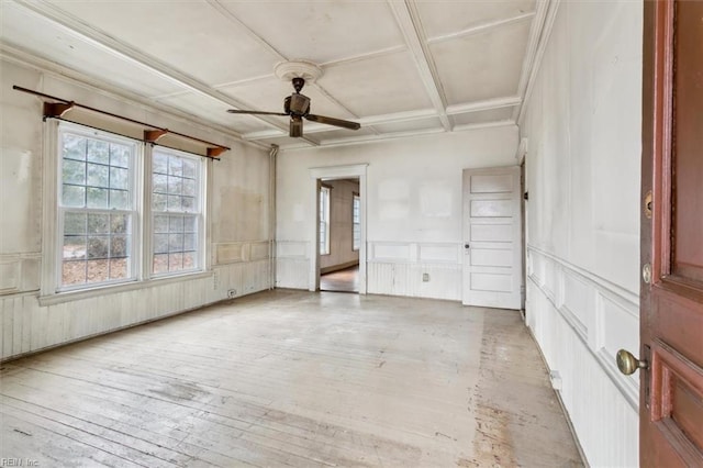 empty room with crown molding, ceiling fan, coffered ceiling, light hardwood / wood-style floors, and beamed ceiling