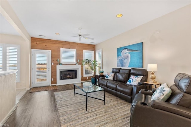 living room featuring ceiling fan, hardwood / wood-style floors, and wood walls