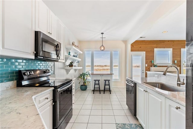 kitchen featuring sink, appliances with stainless steel finishes, wooden walls, pendant lighting, and white cabinets