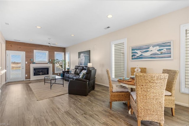 living room with ceiling fan, wooden walls, a wealth of natural light, and light wood-type flooring