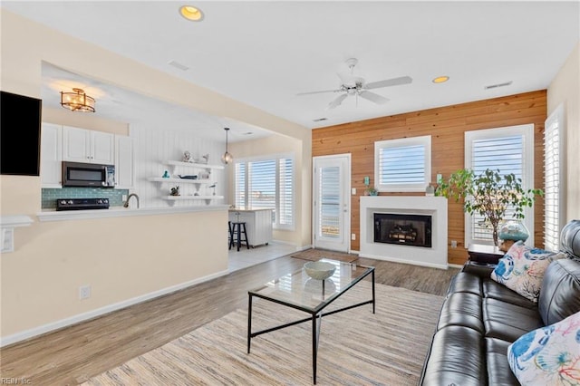 living room with sink, light hardwood / wood-style floors, ceiling fan, and wood walls