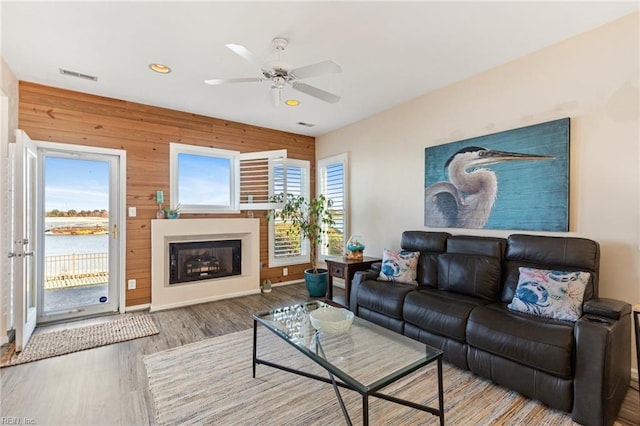 living room with a water view, wooden walls, hardwood / wood-style floors, and ceiling fan