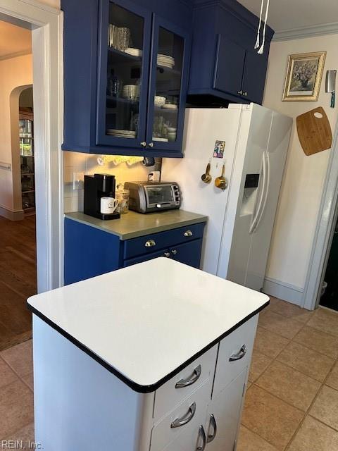 kitchen with crown molding, white refrigerator with ice dispenser, blue cabinetry, and light tile patterned floors