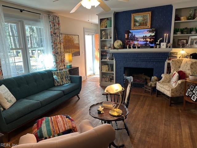 living room featuring a brick fireplace, wood-type flooring, built in features, and ceiling fan