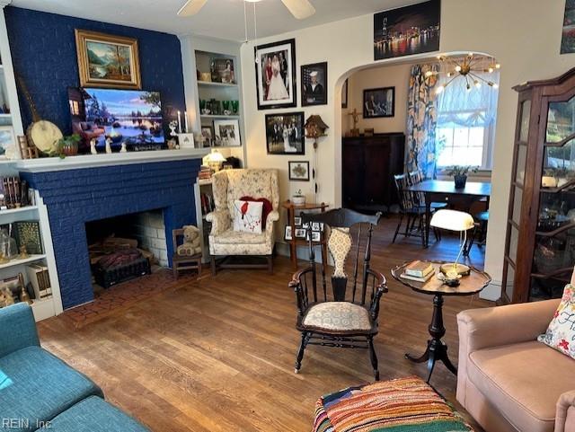 living room featuring built in shelves, ceiling fan, hardwood / wood-style floors, and a brick fireplace