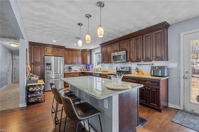 kitchen featuring a kitchen island, decorative light fixtures, a kitchen bar, stainless steel appliances, and light stone countertops