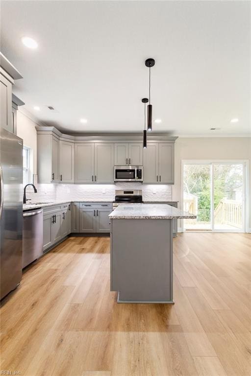 kitchen featuring pendant lighting, gray cabinetry, backsplash, stainless steel appliances, and light stone countertops