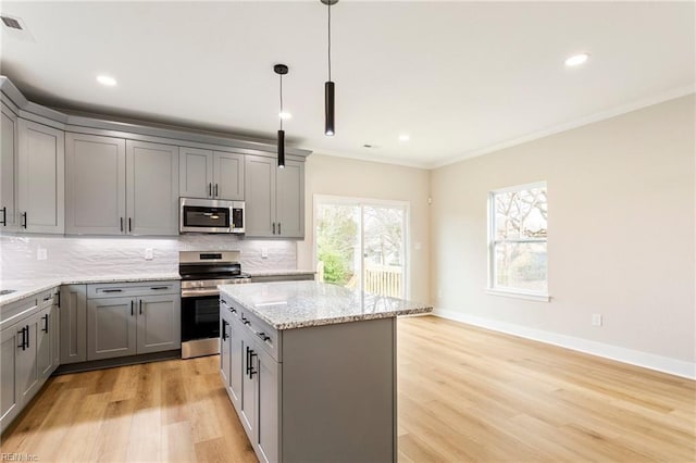 kitchen featuring stainless steel appliances, light stone countertops, a kitchen island, and gray cabinetry